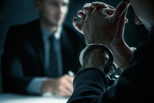 A handcuffed man sitting across from an attorney during an interrogation, representing cases handled by a Tampa misdemeanor defense lawyer.