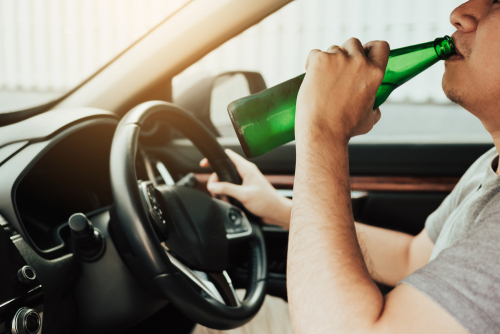 Tampa second offense DUI lawyer represented through a driver drinking from a bottle while behind the wheel, illustrating repeat DUI allegations.