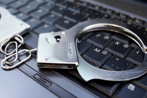 Tampa internet fraud defense lawyer represented through handcuffs resting on a computer keyboard, highlighting charges involving online crimes.