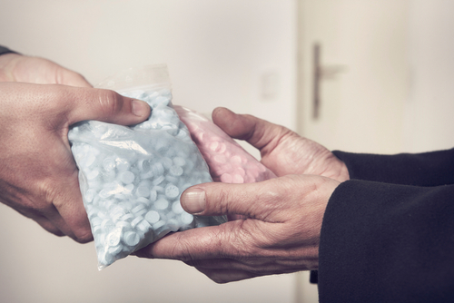Two individuals exchange bags of blue and pink pills, representing cases handled with the support of a Tampa Possession with Intent to Distribute Defense Lawyer.