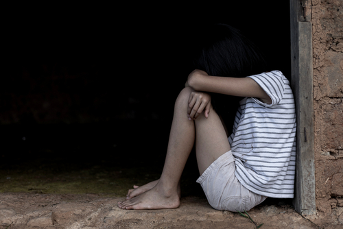 Child sitting alone in a dim doorway with head down, representing sensitive cases handled by a Tampa child molestation defense lawyer.