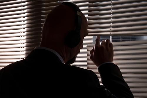 Tampa espionage defense lawyer represented through a man wearing headphones while peeking through blinds, illustrating federal surveillance concerns.