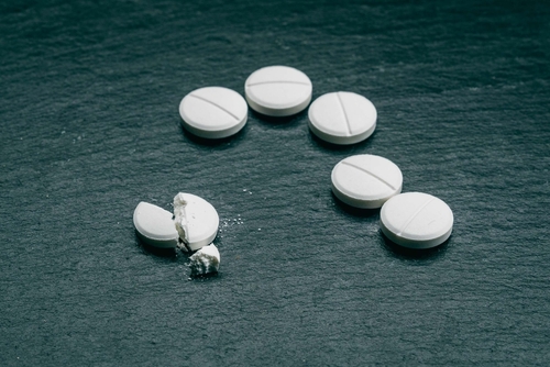 White ecstasy tablets, including a broken pill, on a dark surface, illustrating cases handled with the support of a Tampa Ecstasy Defense Lawyer.