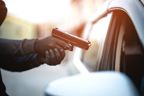 A masked individual pointing a handgun at a driver through a car window, illustrating violent carjacking allegations handled by a Tampa carjacking defense lawyer.