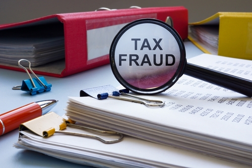 Tampa tax fraud lawyer depicted through a magnifying glass labeled Tax Fraud positioned over financial documents, reflecting IRS scrutiny and allegations of improper filings.