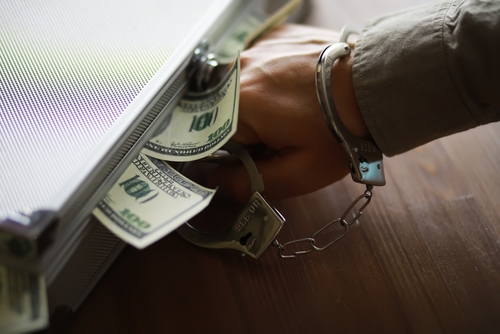 Tampa money laundering lawyer represented through a handcuffed person holding a briefcase stuffed with cash, symbolizing federal financial crime allegations.