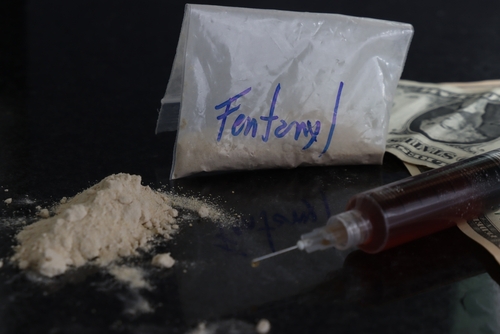 Bag labeled “Fentanyl” beside powder, a syringe, and cash on a dark surface, representing cases handled with the support of a Tampa Fentanyl Possession Lawyer.