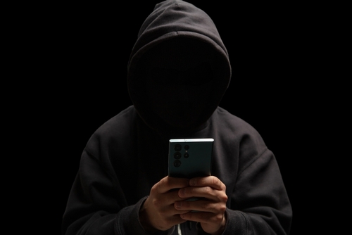 A hooded figure holding a smartphone in the dark, illustrating cases involving threatening communications handled with the support of a Tampa criminal threats lawyer.