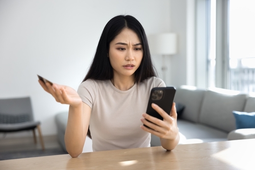 Tampa credit card fraud lawyer represented through a woman looking concerned at her phone while holding a credit card, illustrating potential fraud issues.