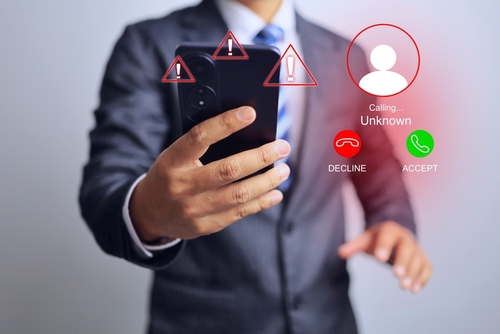Person holding a phone with warning symbols and an unknown caller alert, representing fraudulent communication in Scheme to Defraud cases in Florida.