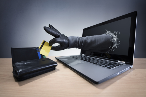 Tampa identity theft lawyer illustrated through a gloved hand reaching from a laptop to grab credit cards, highlighting digital theft allegations.