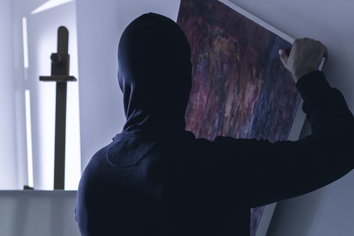 A hooded individual removing a framed painting from a wall, representing theft-related allegations handled by a Tampa theft crime lawyer.