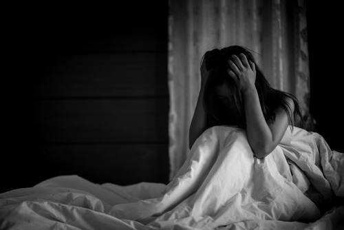 A distressed person sitting on a bed with their head in their hands in a dimly lit room, symbolizing sensitive cases handled by a Tampa sexual battery lawyer.