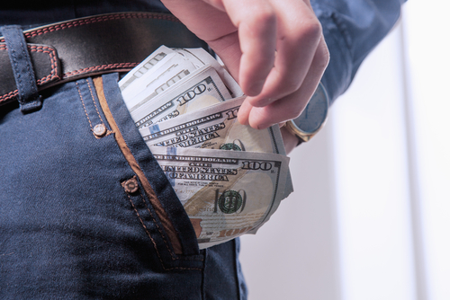 Hand placing a bundle of hundred-dollar bills into a pocket, representing financial theft allegations handled by a Grand Theft defense lawyer.