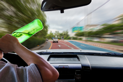 Tampa third offense DUI lawyer represented through a driver holding a green bottle while speeding on the road, illustrating repeat DUI risks and felony-level consequences.